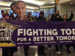 Commercial office janitors, retail janitors, security officers, window cleaners, and airport workers march through the downtown Minneapolis skyway, carrying a banner that reads "Fighting Today for a Better Tomorrow," as part of SEIU Local 26's contract campaign.