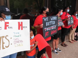 A woman holds a sign about Work from Home, while a child and a group behind her hold other signs.