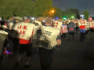 A crowd of workers walk away from the camera at night wearing tabards reading “District Lodge 70 on strike”