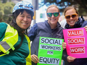 Three women hold signs saying “Social Wokrers for Equity” and “Value Social Work”