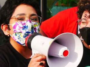 One masked worker speaks into a bullhorn as another looks on. Both look happy and young.