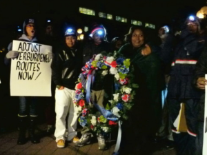 People in postal gear stand in the dark holding hand-lettered signs: "END DELIVERY IN THE DARK," "ADJUST OVERBURDENED ROUTES NOW," REOPEN MAIN PROCESSING PLANTS" and a memorial wreath.