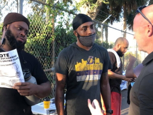 Sean O'Brien (right), a bald white man, speaks as two workers, Black men, listen. One worker is holding a Teamsters United flyer. Behind them is a chain-link fence and someone in a UPS delivery uniform.