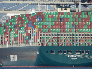 Huge ship loaded with containers, viewed from stern which says "Ever Given, Panama." In the background are port cranes.