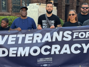 A group of veterans stand behind a blue banner that reads Veterans for Democracy.