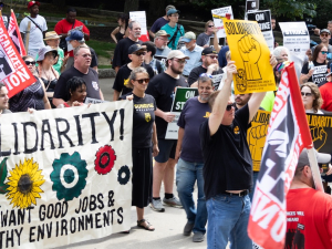 A rally with 30 or so people with a mixture of colorful signs, including Painters Union and a “We Want Good Jobs and Health Environments” banner