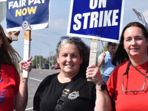 Three women smile at the camera with UAW on Strike signs.