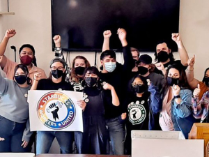 A crowd of Starbucks workers and other Workers United members celebrate with arms raised, posing for photo