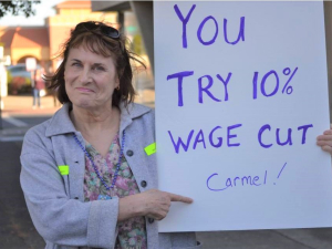 woman outdoors holds sign: "You try 10% wage cut Carmel!"