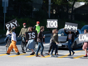 grad students blocking traffic in the street with signs that read "The Pay Is Too Damn Low"