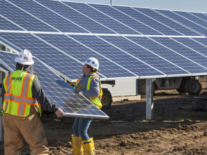 Three solar workers in yellow vests lift a large solar panel into place on a solar array.