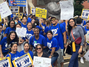 A group of 25 fired-up nurses in royal blue t-shirts poses with signs about striking and safe staffing.