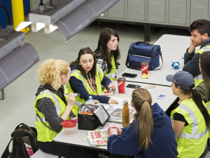 Workers in yellow vests sit around a lunch table at work.