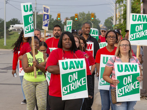 GM strikers march with "UAW on strike" signs. Black and white women in foreground.