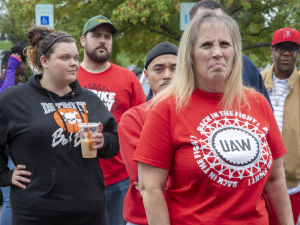 A determined-looking woman with a crowd behind her wears a red shirt saying UAW, Back in the Fight