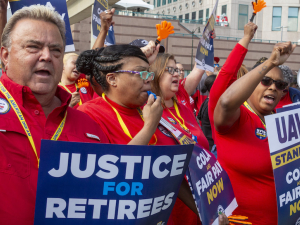 Auto workers in red shirts hold signs, including “justice for retirees”