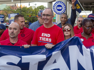 A group of men and women in red T-shirts stand holding a blue banner, the word ‘Stand’ is visible.