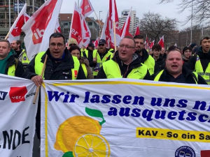 People with red flags march behind a banner adorned with lemons.