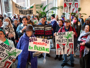 A group of forty cram into a building lobby with signs saying “Labor for Palestine”