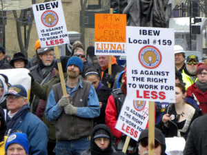 Warmly dressed people march with LIUNA and IBEW union signs opposing "Right to work for less" in Wisconsin.