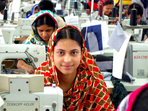 Bangladeshi garment worker at sewing machine looks up, sitting in factory