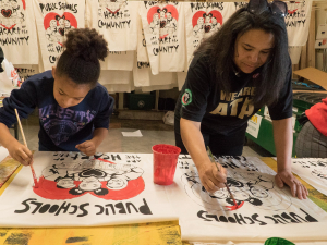 Two people painting signs that say "public schools are the heart of the community"