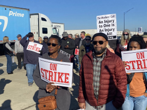 A group of workers and supporters hold signs that read STRIKE in front of a blue Amazon Prime truck.