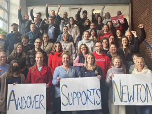 Two dozen teachers stand on stairs with signs saying ‘Andover Supports Newton’