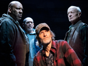 Four actors on stage in front of a black background.