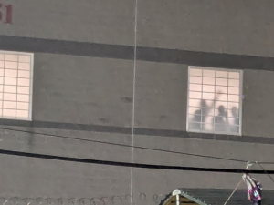 A photo taken at night shows detainees silhouetted in the prison window, one with fist raised. 