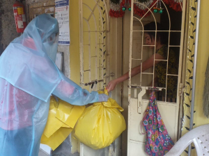 Dalit sanitation worker in a PPE suit accepting trash in yellow bags by hand from the home of a coronavirus patient