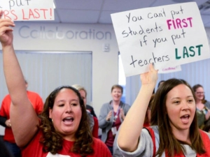 Two teachers holding signs. Tiffany's sign says "You can't put students first if you put teachers last."