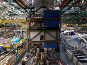 An aircraft factory floor is viewed from above, with planes on either side and high rafters above.