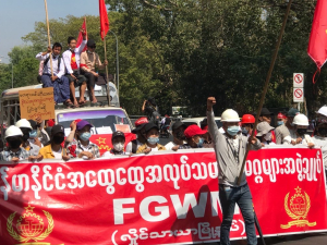 Dozens of workers march behind a red banner in Myanmar. Some carry red flags.