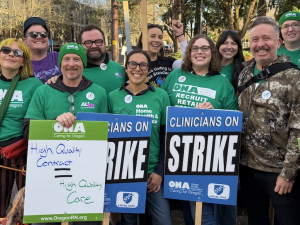 A group of green-shirted union members hold strike signs and smile.