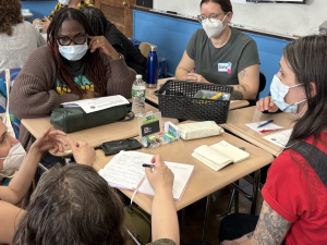 A group of masked people sit around a table discussing something intensely.