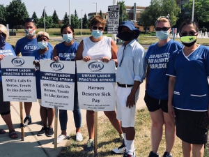 Nurses hold picket signs that read "AMITA: Calls Us Heroes, Treats Us Like Zeroes," in front of St. Joseph Hospital.