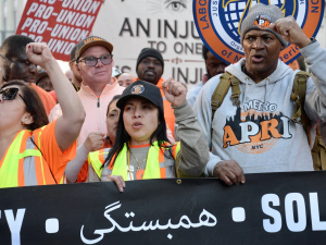 Members of the Laborers Union march during the May Day rally in New York City, behind a black banner that says solidarity in multiple languages, including Arabic.