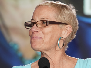 Photo of Jane McAlevey smiling at a microphone and looking left in an aqua blue shirt