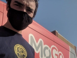 A bikeshare driver wearing a black mask stands in front of a red MoGo van.