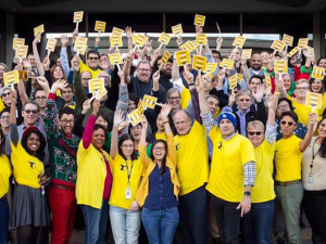 NewsGuild members standing together in yellow, smiling holding signs with arms up