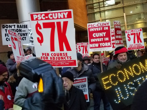 crowd holding signs including "PSC-CUNY $7k per course for adjuncts," "invest in CUNY, invest in New York," and "ECONOMIC JUSTICE" spelled out in lights