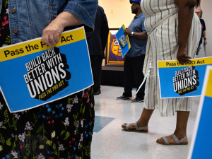 Several woman hold blue and yellow signs that read "Pass the Pro Act: Build Back Better with Unions."