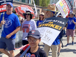 Actor Sam Humphrey and several others march towards the camera with ‘SAG AFTRA on strike’ and ‘Writers Guild of America On Strike’