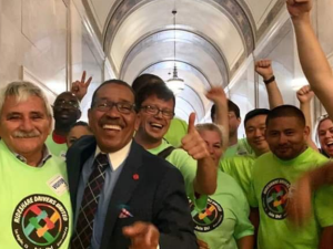 Happy people in neon yellow RDU shirts, plus a man in a suit, raise jubilant fists in a legislative hallway