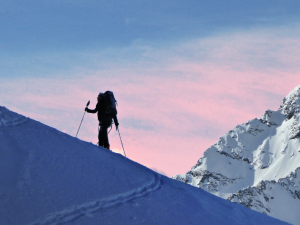 Silhouette of a skier ascending a mountain slope with pink sky in background