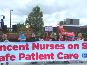 People outside hold a huge banner: "St. Vincent Nurses on Strike for Safe Patient Care; MNA"