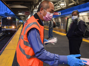 Man in orange vest hands out masks inside a train station