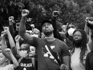 Black and white photo of a crowd people, mostly Black, various ages, all with fists raised in the air.