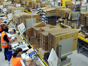 Amazon warehouse with goods on shelves and workers in orange vests working.